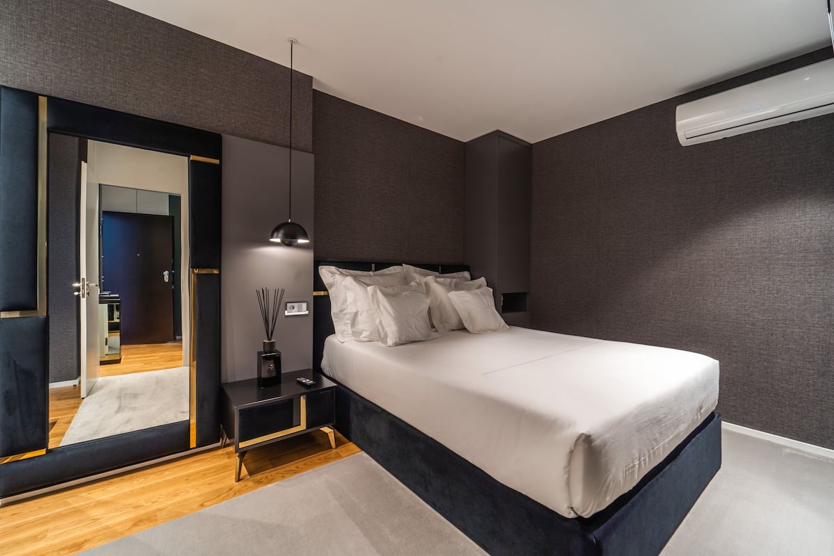 A modern bedroom with a large bed, a bedside table, a mirror, and a hanging light fixture.