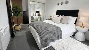 Un dormitorio con cama, mesita de noche, lámpara y espejo.