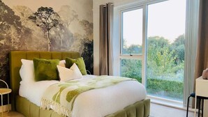 Ein Schlafzimmer mit einem großen Bett, Blick ins Grüne durch das Fenster und einem Wandgemälde.