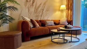 Ein gemütliches Wohnzimmer mit braunem Sofa, einem runden Couchtisch und einem großen Fenster mit Vorhängen.