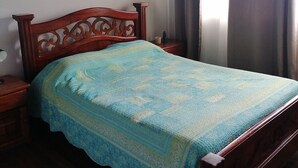 Ein Schlafzimmer mit einem hölzernen Bett, einem Nachttisch, einem Beistelltisch und einem Fenster mit Vorhängen.