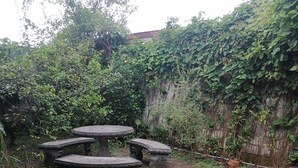 Ein Innenhof mit Steintisch und Bänken, umgeben von dichtem Grün und einer hohen Mauer.