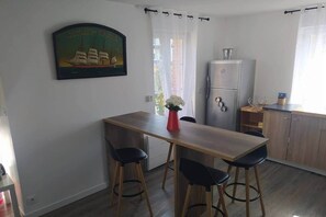 A small kitchen with a wooden table, two bar stools, a refrigerator, and a decorative sign on the wall. - Apartment with a garden and parking (Saint-Malo)