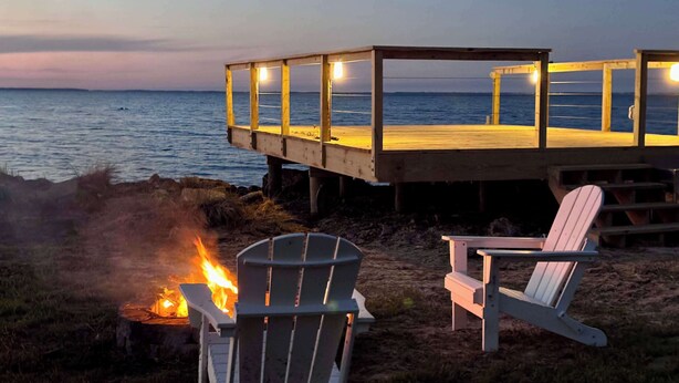 Une terrasse en bois donnant sur l’océan, avec deux fauteuils Adirondack et un foyer extérieur.