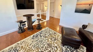 Un salon moderne avec un plancher en bois, un canapé en cuir noir, un tapis à motifs et un téléviseur fixé au mur.