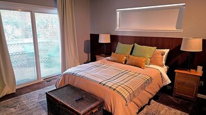 Quarto de hotel com uma cama grande, duas mesas de cabeceira, uma mesa de apoio, uma janela com cortinas e vista para o exterior.