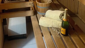 Et sauna rum med trævægge, en bænk, en spand, en champagneflaske og to glas.