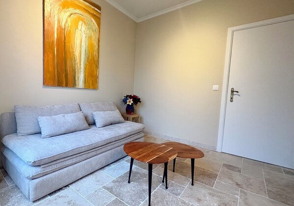 A living room with a sofa, two wooden tables, a painting on the wall, and a door.