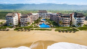 A resort with multiple buildings, a central pool, and a beach in the foreground. - 1-bedroom Ocean view Condo in Vivo Resorts, Puerto Escondido, Gym & Tennis Court (Bajos de Chila)