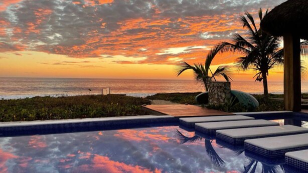 A swimming pool with a sunset view, lounge chairs, and a palm tree. - 1-bedroom Ocean view Condo in Vivo Resorts, Puerto Escondido, Gym & Tennis Court (Bajos de Chila)