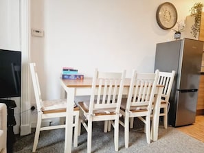 A dining area with a wooden table and four chairs, a television, a refrigerator, and a wall-mounted clock. - Heart Of Alba (Edinburgh)