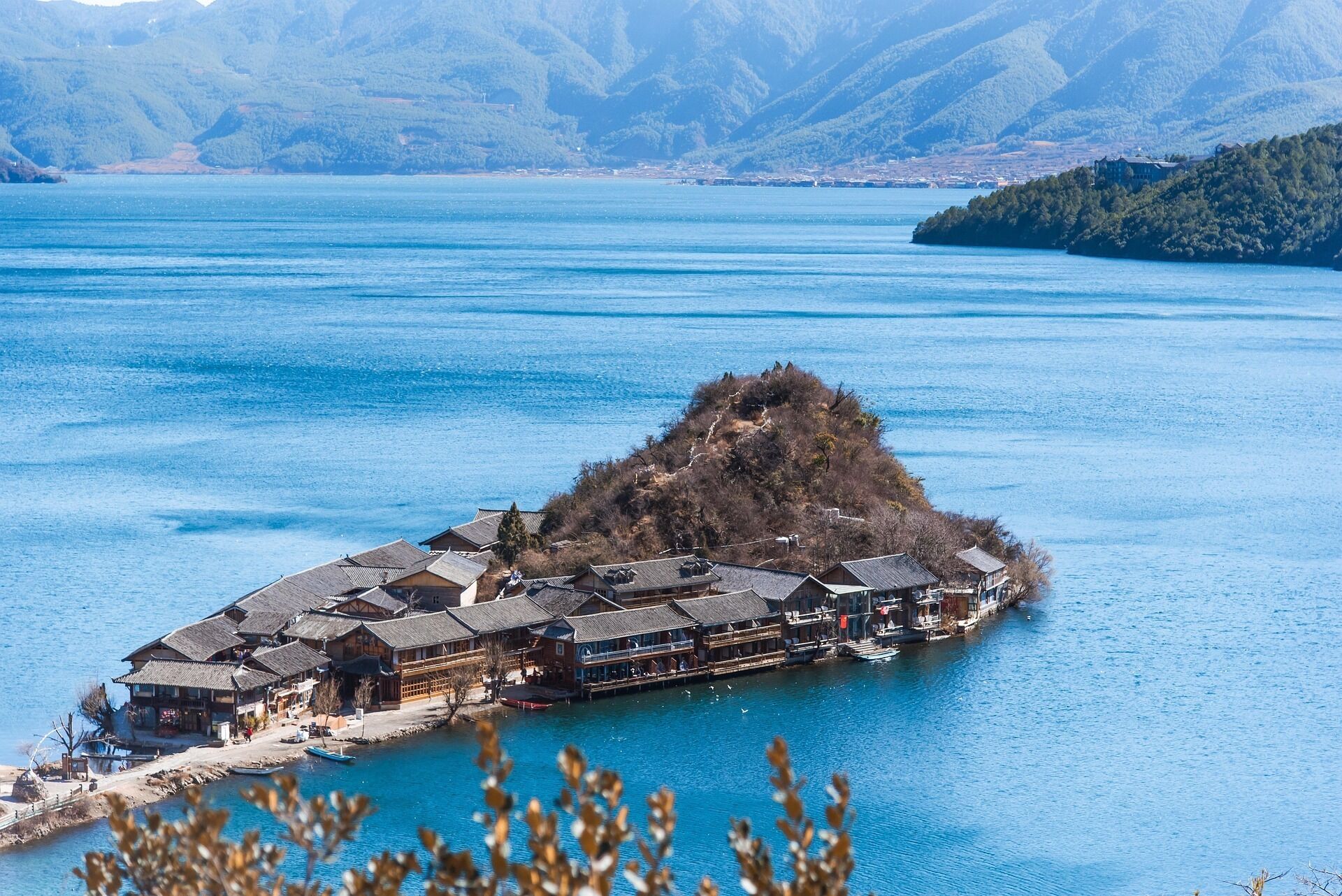 A traditional wooden building with multiple levels and a steep roof, situated on a small island in a large body of water.