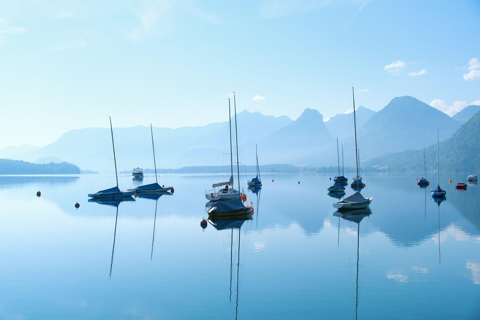 Un lac paisible où plusieurs voiliers sont amarrés, entouré de montagnes sous un ciel dégagé.