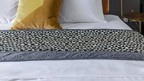 Siististi pedattu sänky, jossa on kuviollinen vuodevaatteisto, pääty ja kaksi tyynyä.