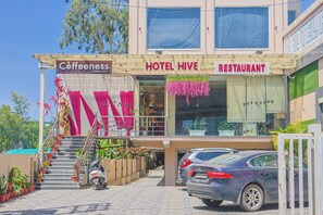 Ein Hotel mit Café und Restaurant im Erdgeschoss, ausgestattet mit einer Treppe mit Blumentöpfen und einem parkenden Auto.