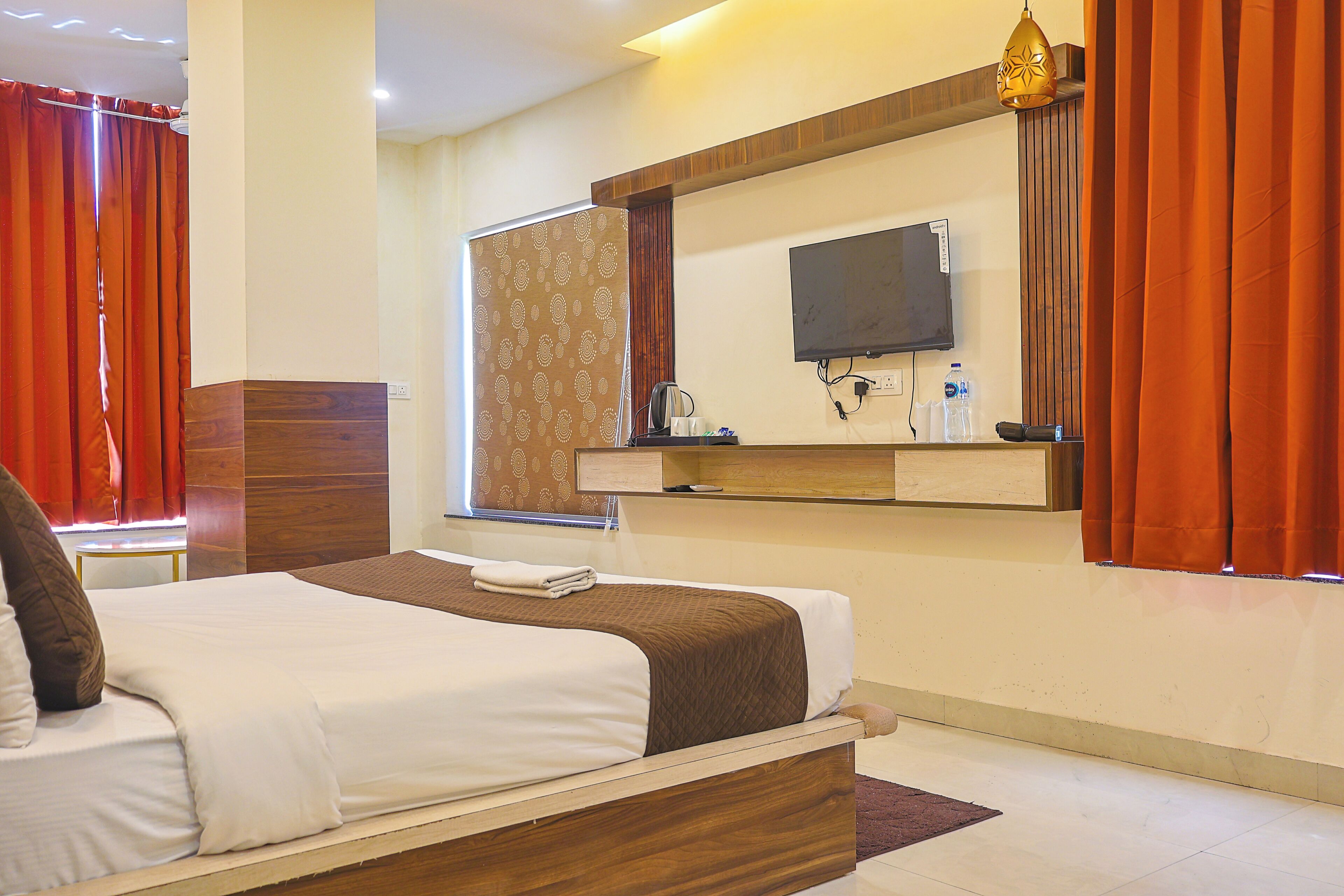 A hotel room with a bed, a television mounted on the wall, a desk with a chair, and a window with curtains.