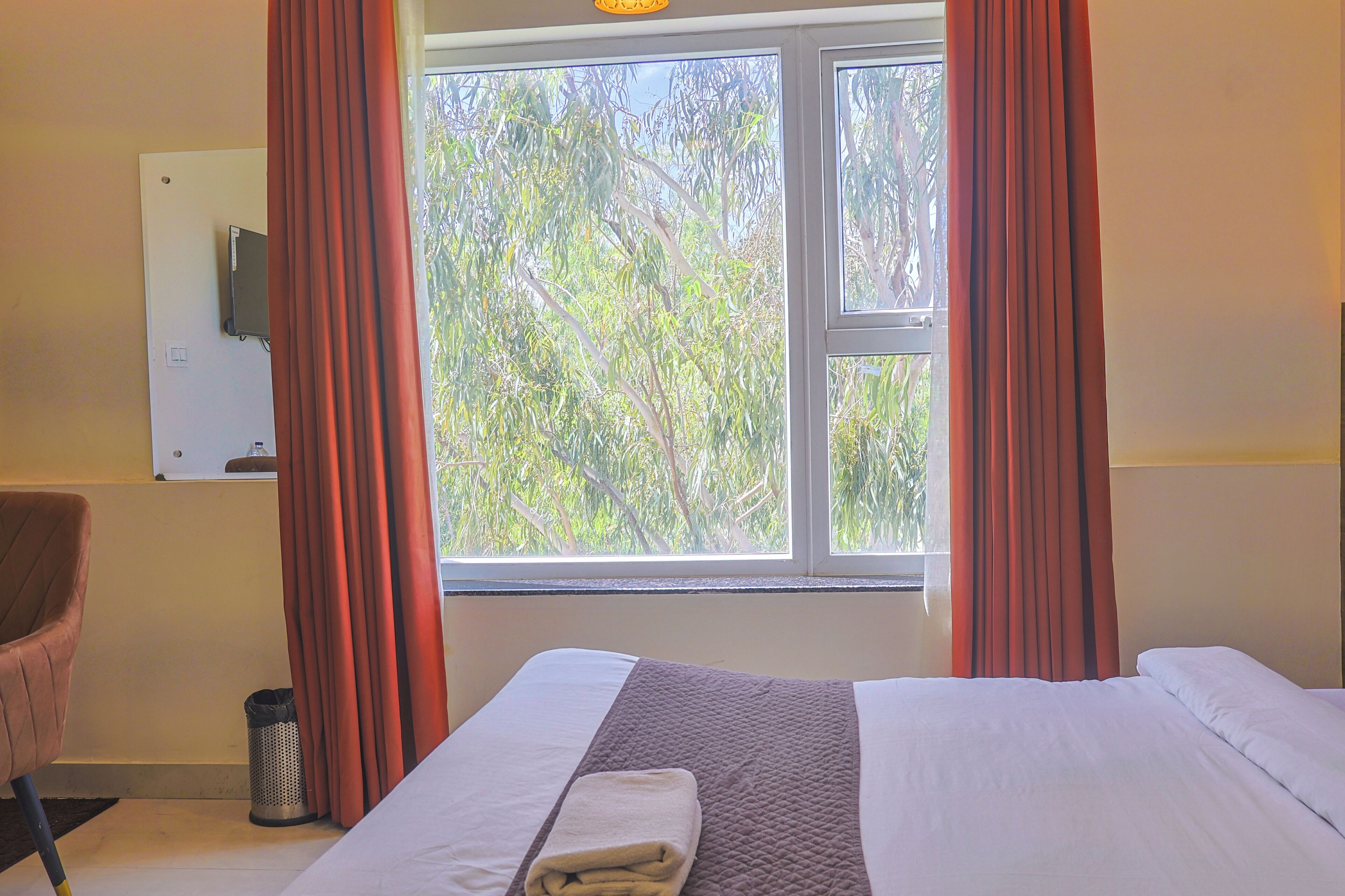 Habitación de hotel con cama, una silla, ventana con cortinas y televisor montado en la pared.