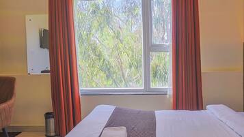 Habitación de hotel con cama, una silla, ventana con cortinas y televisor montado en la pared.