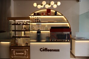 Ein Café namens 'Coffeeness' mit einer Glastheke, Regalen für Kaffeeprodukte und einer Kaffeemaschine.
