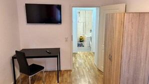 Una habitación con un televisor de pantalla plana en la pared, un escritorio negro con una silla y un armario de madera.