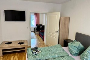 Une chambre à coucher comprenant un lit, un téléviseur, une table en bois avec un jeu d’échecs et une armoire.