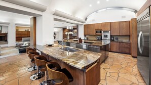 Une cuisine moderne dotée d’un grand îlot central, d’appareils électroménagers intégrés et d’un sol carrelé en pierre.