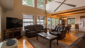 A spacious living room with leather sofas, a large flat-screen TV, and a dining area with wooden furniture. - Peaceful Point Waterfront Dogs Welcome, Near Acadia National Park & Bar Harbor (Eddington)