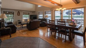 A spacious living room with a fireplace, a dining area with wooden chairs, and large windows offering a view of the outdoors. - Peaceful Point Waterfront Dogs Welcome, Near Acadia National Park & Bar Harbor (Eddington)