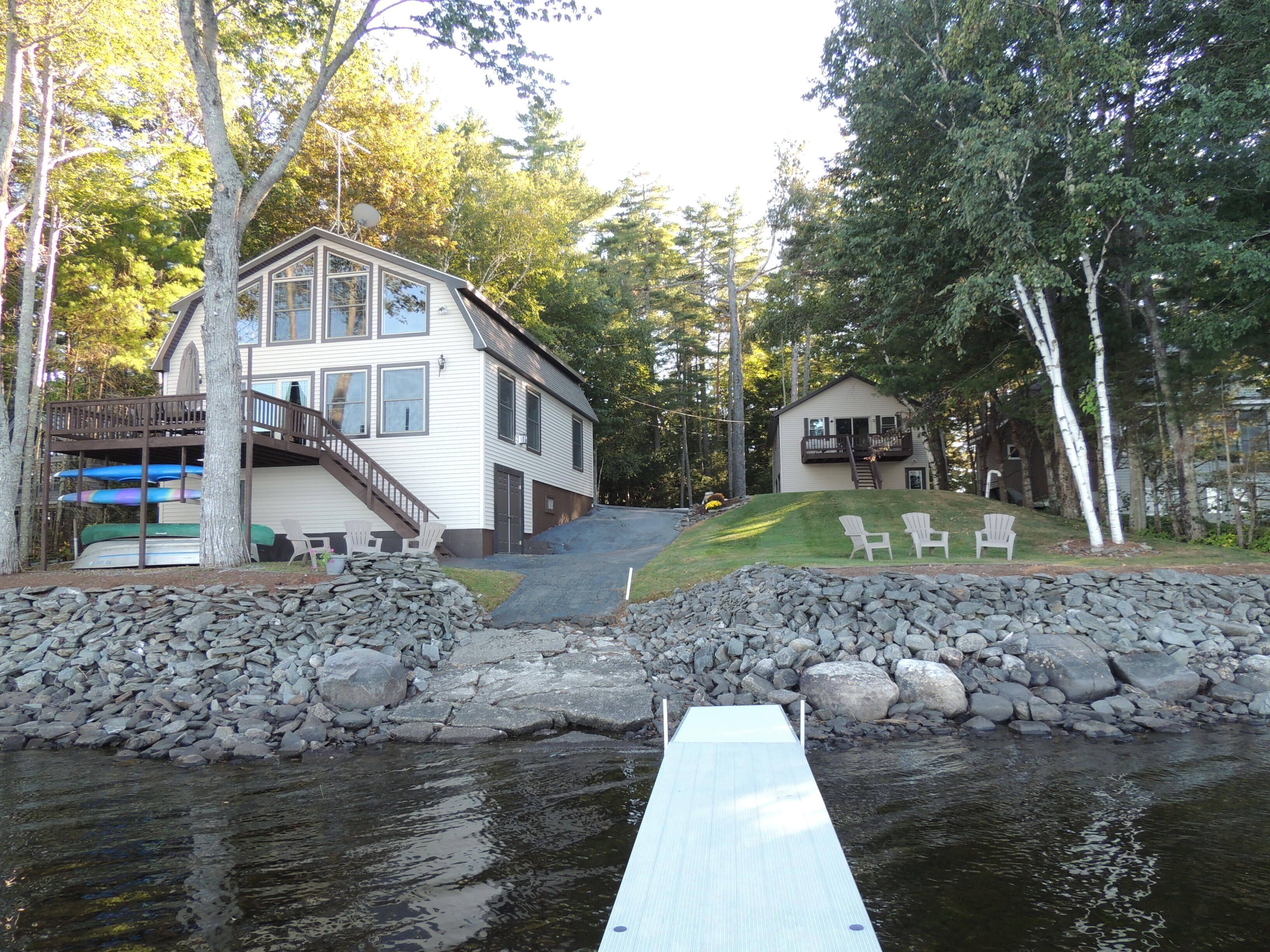 A lakeside cabin with a dock extending into the water, surrounded by trees and a stone wall.