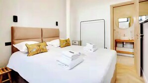 Une chambre d’hôtel avec un grand lit, une table de chevet, un miroir et une salle de bain visible à travers une porte ouverte.