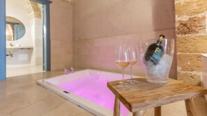Et badekar med rosa lys, to glas hvidvin og en champagneflaske på et træbord.