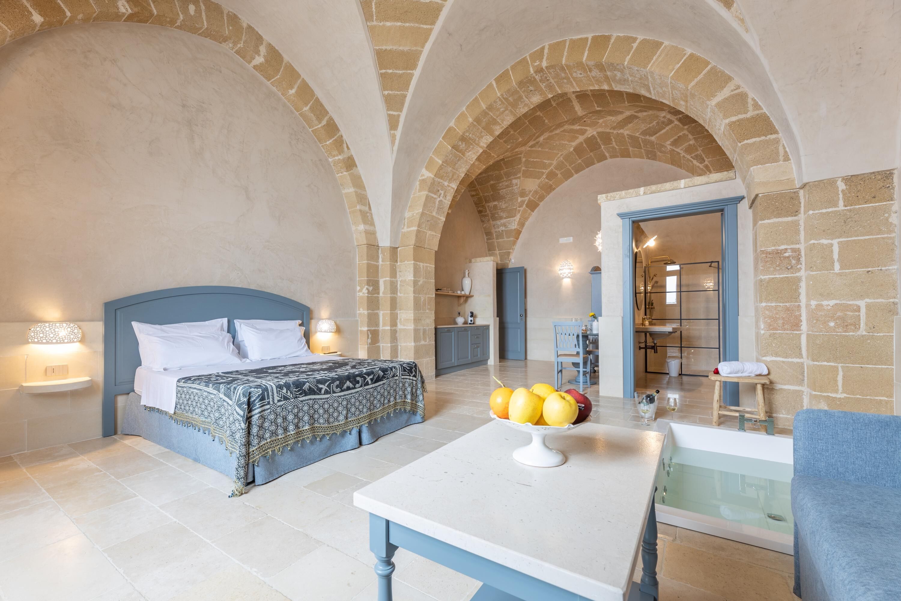 Une chambre à coucher avec un lit, une table avec des fruits, une baignoire et une salle de bain avec un lavabo et un miroir.