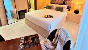 Una habitación de hotel con una cama grande, una mesita de noche con una revista, una lámpara y un espejo montado en la pared.