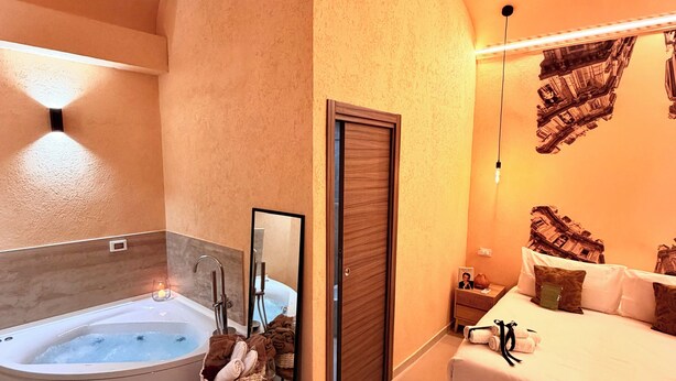 Un baño moderno con una bañera independiente, un tocador con espejo, y una cama con almohadas y toallas.