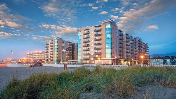 Ein Strandhotel mit mehreren Etagen, Balkonen und einem Sandstrand im Vordergrund.