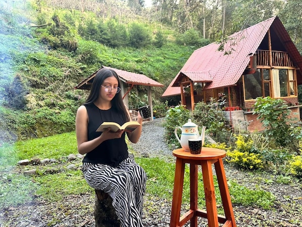 Une personne est assise à l’extérieur, en train de lire un livre, avec une table et une théière à proximité.