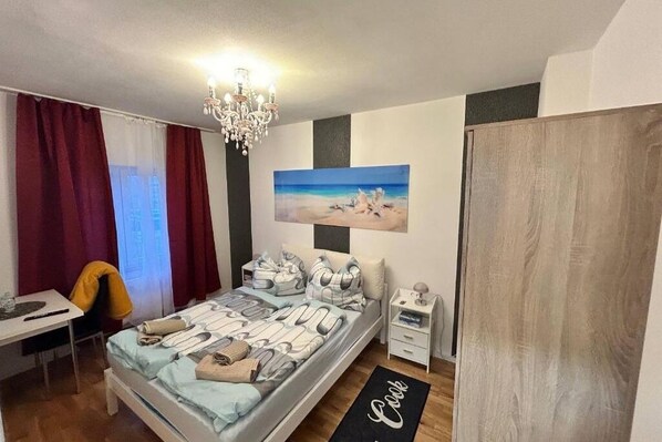 A bedroom with a bed, a desk, a chair, a chandelier, a painting, and a wardrobe. - Casa Delli Gatti - Modern apartment with 1 bedroom and sunny balcony (Leipzig)