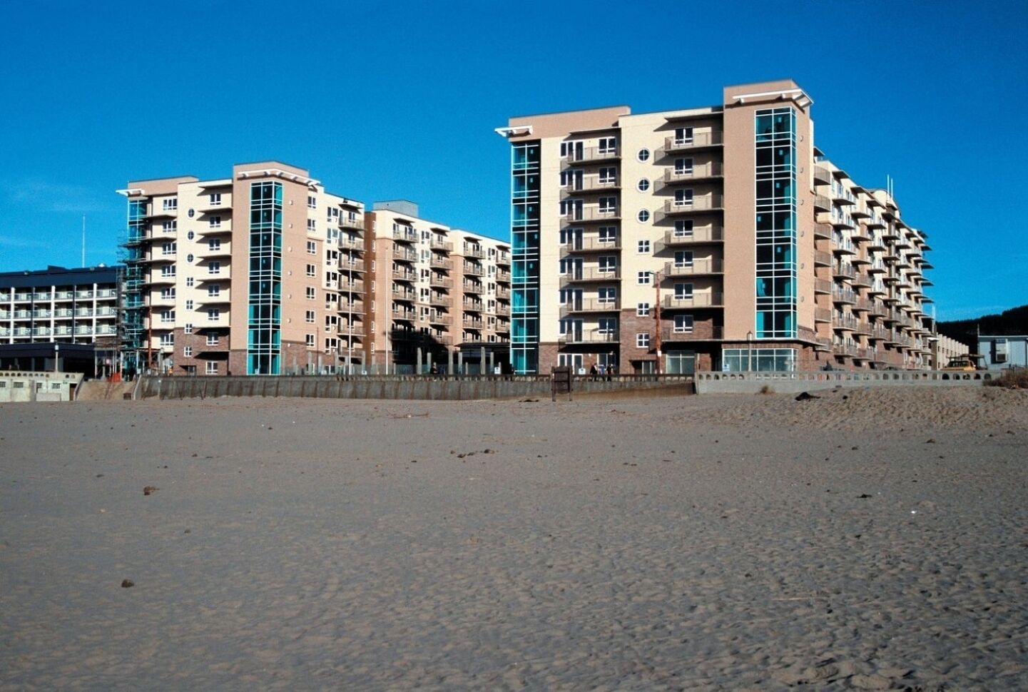 A beachfront hotel with multiple floors, balconies, and a sandy beach in the foreground.