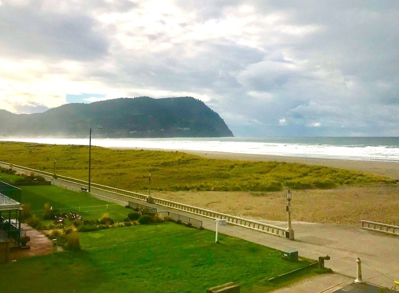 A coastal view with a beach, grassy areas, and a distant mountain.