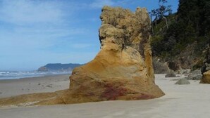 Une grande formation rocheuse sur une plage, sous un ciel dégagé.