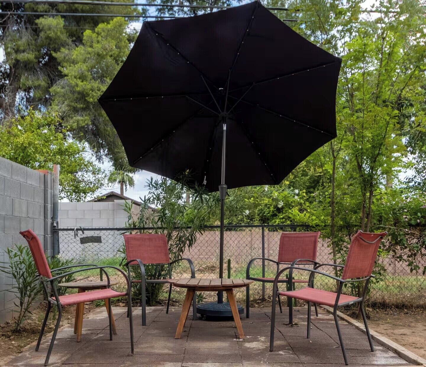 A patio with a large black umbrella, four metal chairs with red cushions, and a small wooden table.