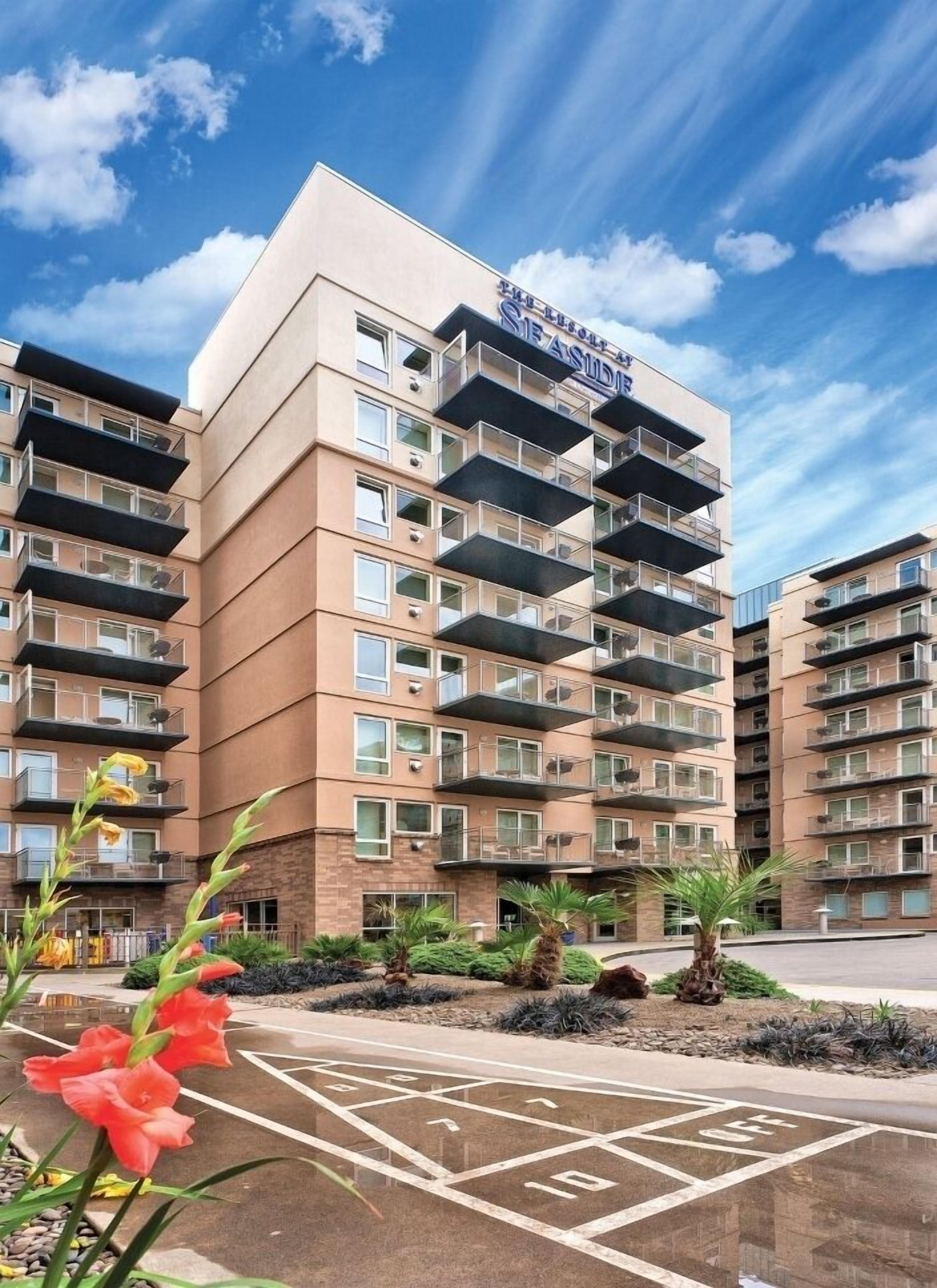 Un hotel de varios pisos con balcones, estacionamiento y cielo despejado.