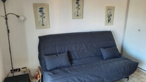 Ein Zimmer mit einem dunkelblauen Sofa, einer Stehlampe und drei gerahmten Blumenbildern an der Wand.