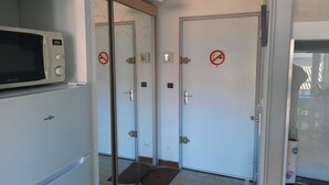 Ein schmaler Flur mit weißen Türen, einer Mikrowelle und einem Kühlschrank.