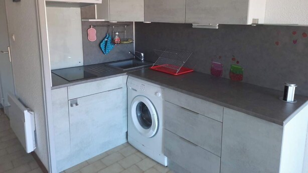 Eine kleine Küche mit integriertem Waschmaschine, Spüle und einer Arbeitsplatte.