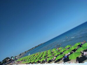 A beach with rows of green umbrellas and people swimming in the water. - Elegant Detached House in the City Center (Avola)