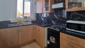 A kitchen with wooden cabinets, a black countertop, a stove, and a microwave.