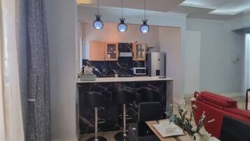 Cocina moderna con encimeras de mármol, comedor con una mesa y sillas negras, y un sofá rojo.