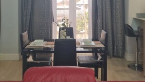 A dining area with a table set for two, a red sofa, and a view through a window with curtains.