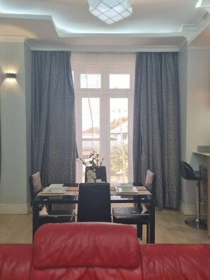Un comedor con una mesa preparada para dos, un sofá rojo y una vista a través de una ventana con cortinas.